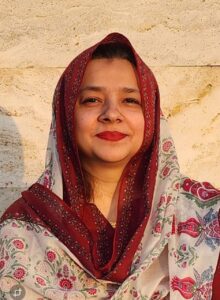 Professional South Asian female Urdu teacher wearing a hijab, smiling confidently in front of plants — expert online tutor at MyUstaza.