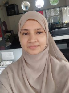 Professional Australian female Islamic scripture teacher wearing a hijab, smiling confidently in front of plants — expert online tutor at MyUstaza.